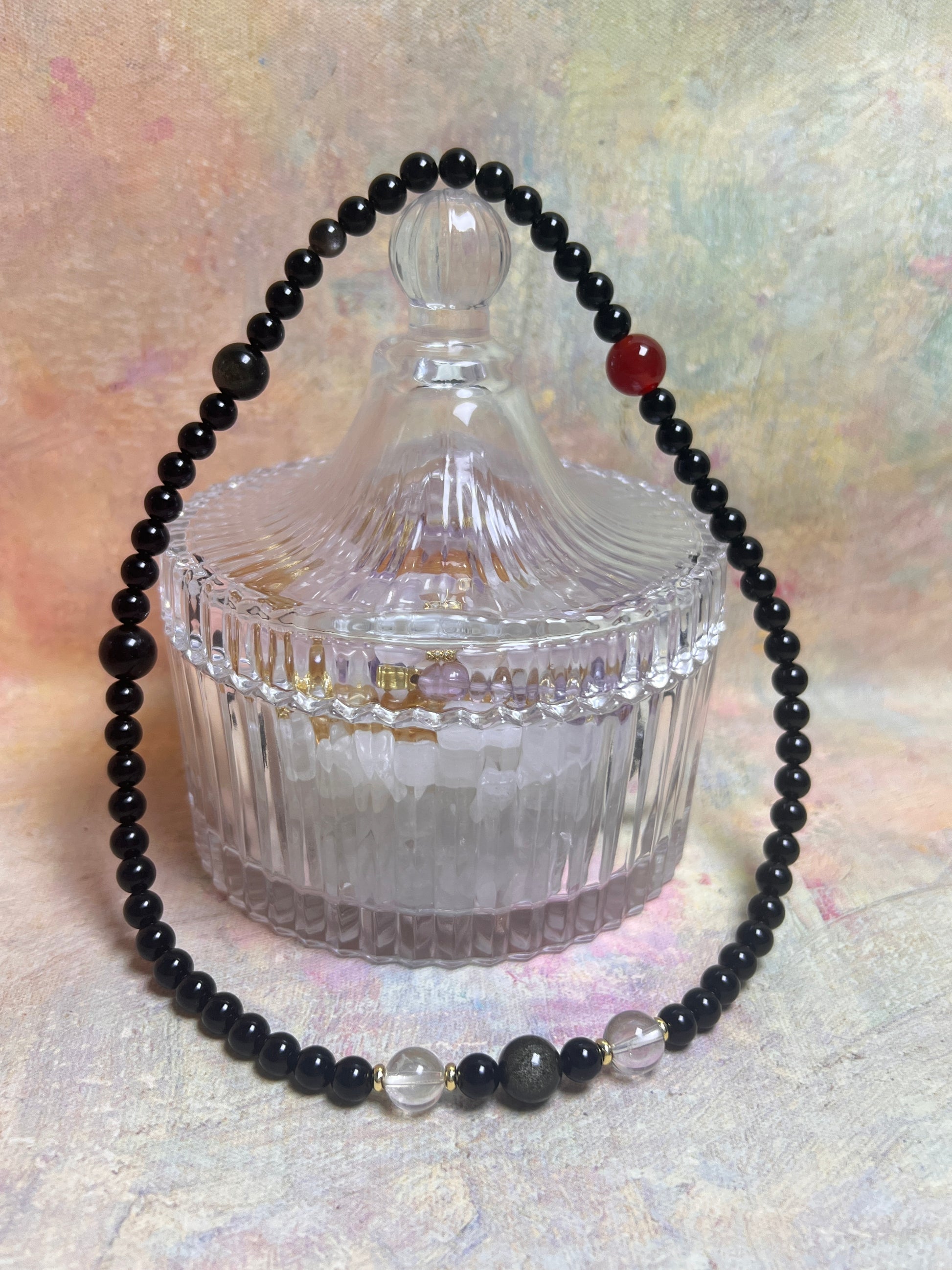 Black beaded bracelet draped over a clear glass container on a textured surface